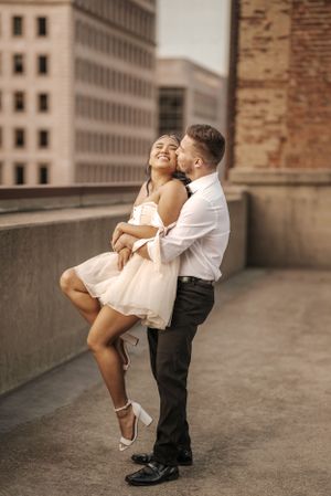 Couple in formal wear embracing on urban rooftop during engagement photoshoot.