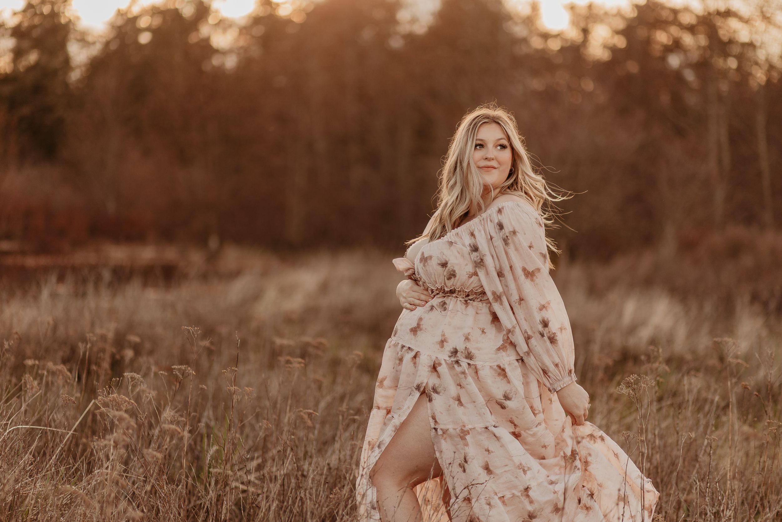 Woman in flowing white dress walking through golden field at sunset.