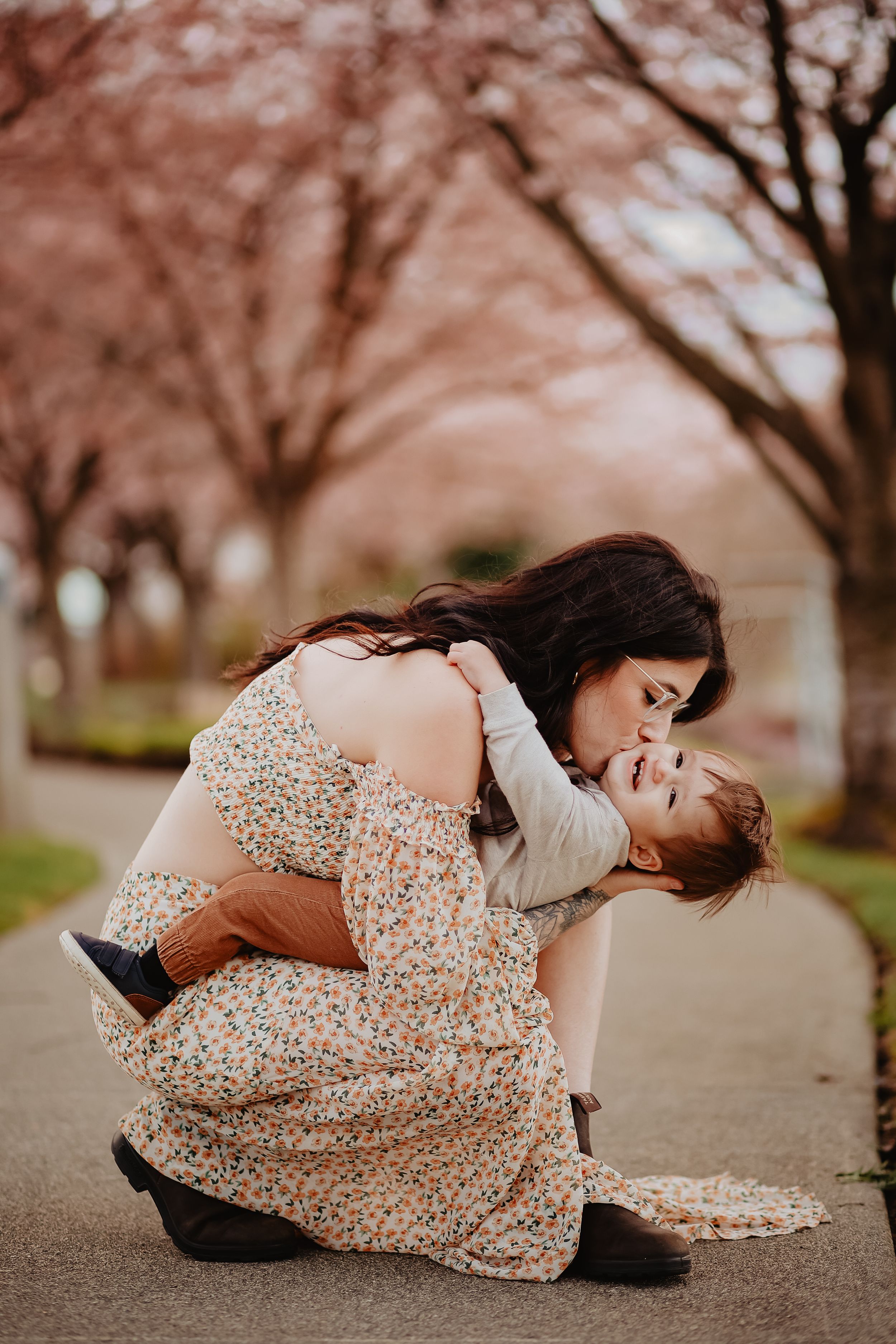 Two people in floral dress lying on ground under cherry blossom trees.