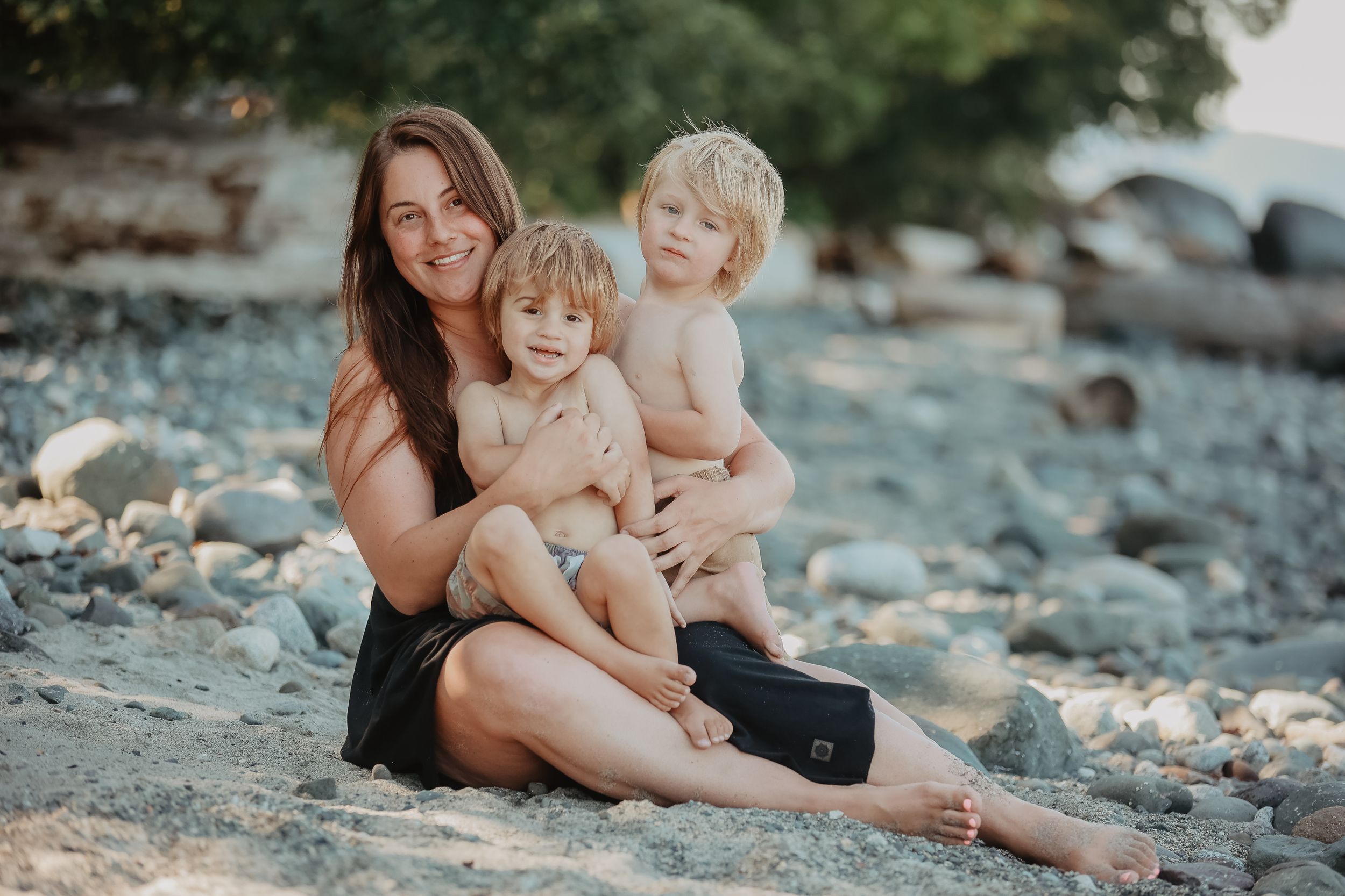 Family sitting together on rocky beach shore during golden hour.