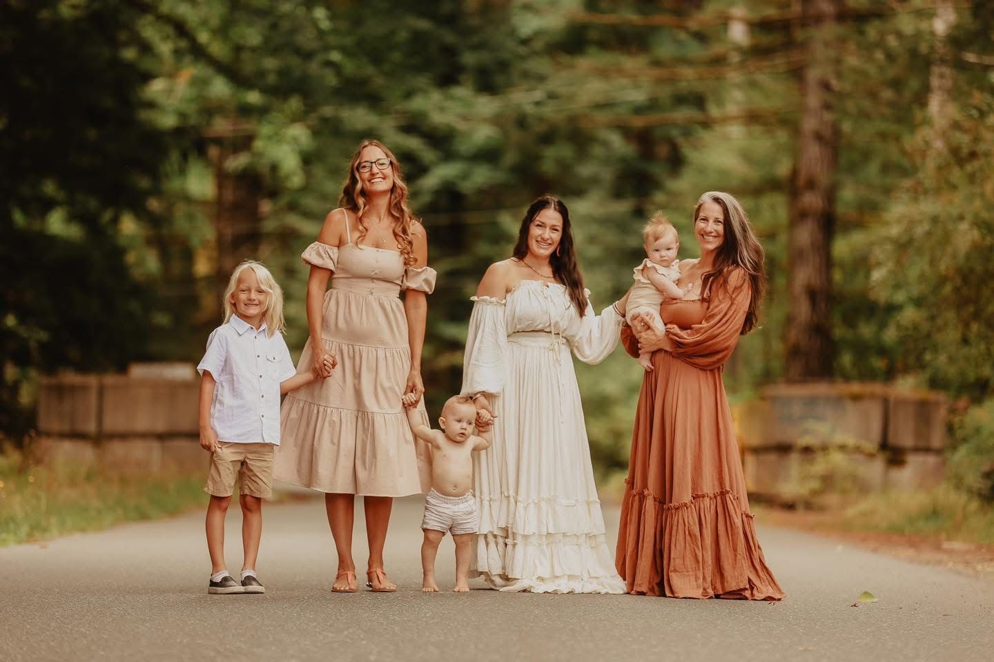 Group wearing coordinated earth-tone dresses standing together on wooded path.