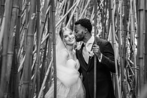 A romantic black and white wedding photo of newlyweds sharing an intimate moment among tall bamboo stalks.