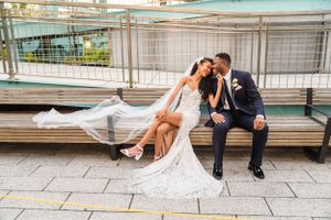 Romantic couple shares an intimate moment sitting on wooden bench in white wedding attire with flowing veil.