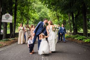 Wedding party walks down tree-lined path outdoors on warm summer day.