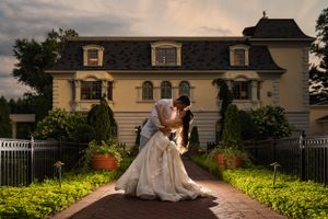 Romantic couple embraces in an elegant dip pose outside a grand manor house at sunset with manicured gardens.