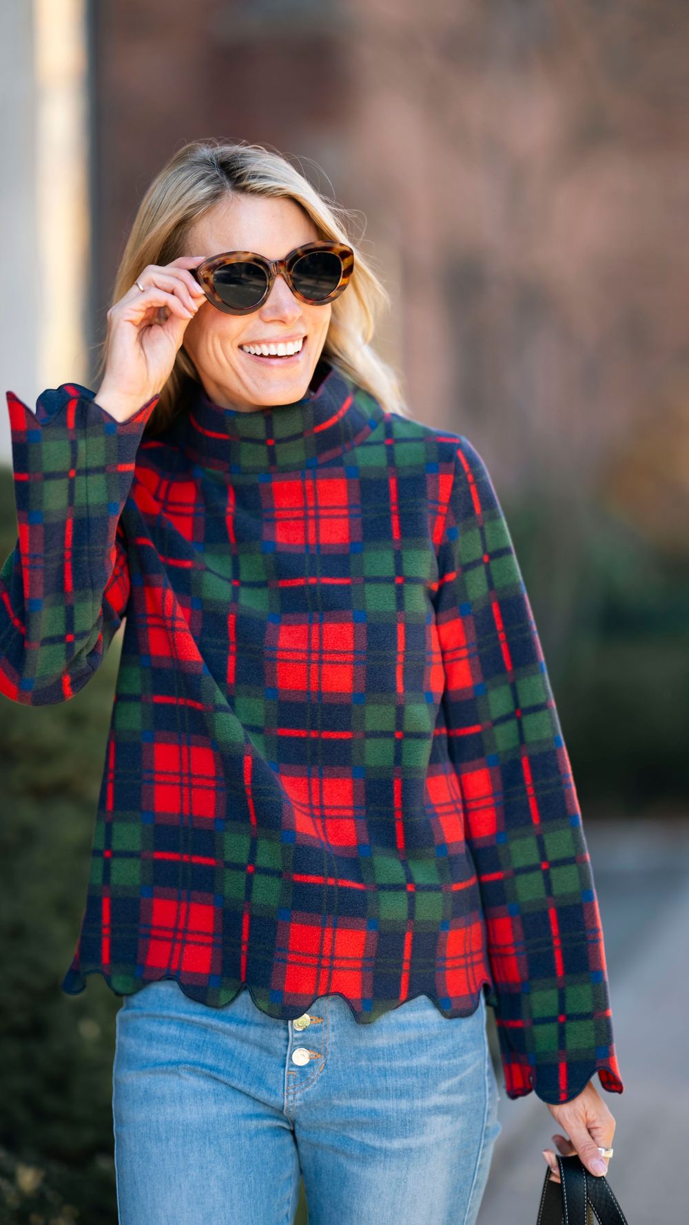 Person wearing plaid fleece pullover and sunglasses on brick-lined street.