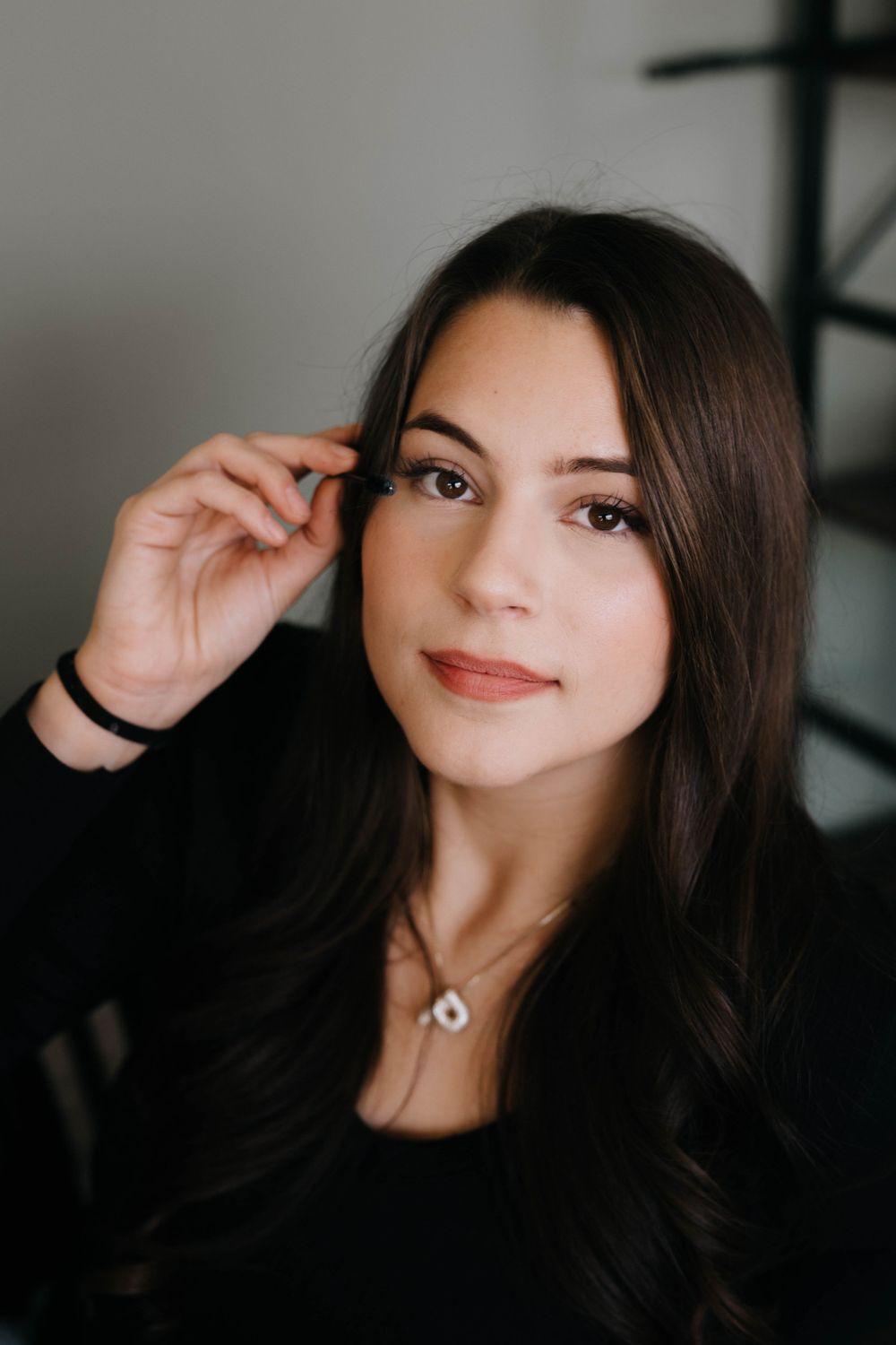 Portrait of a woman with long dark hair wearing a black top and necklace, looking at camera with a gentle smile.