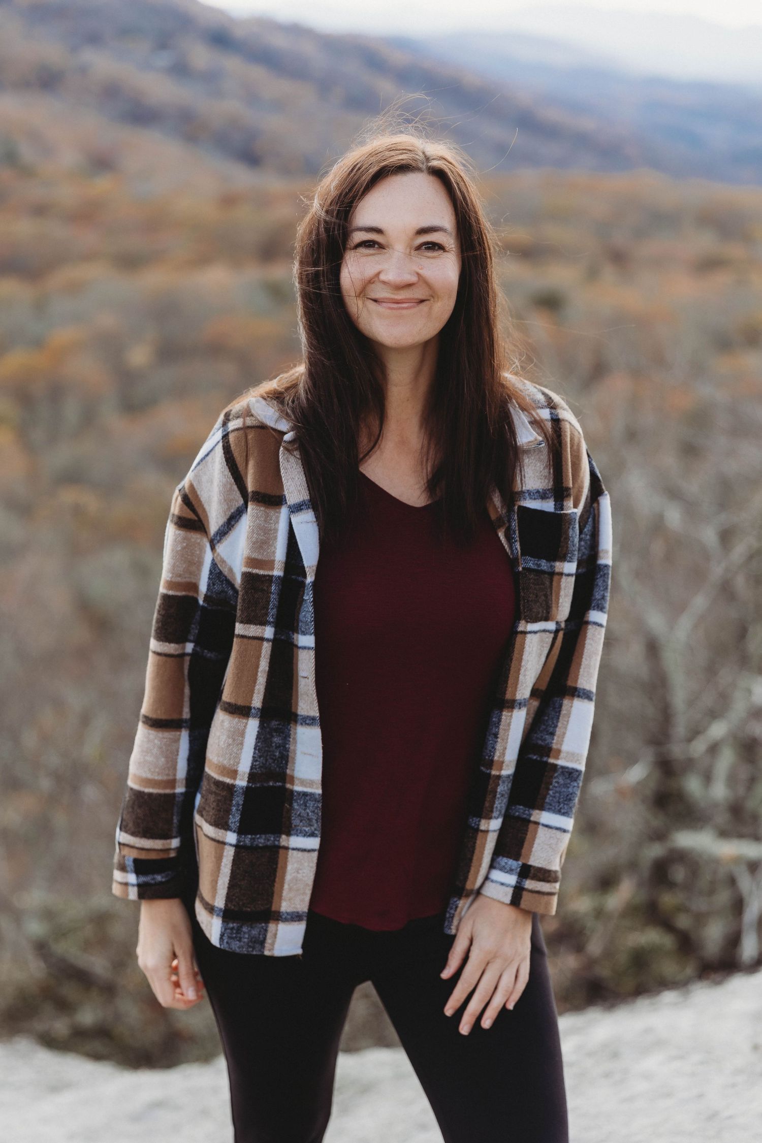 Portrait series of someone wearing a plaid flannel shirt and burgundy top against a mountain backdrop.