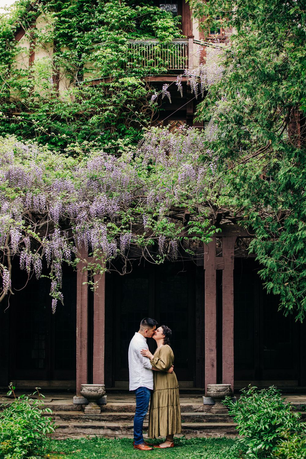 A romantic couple sharing an intimate moment under blooming wisteria in a garden pergola.