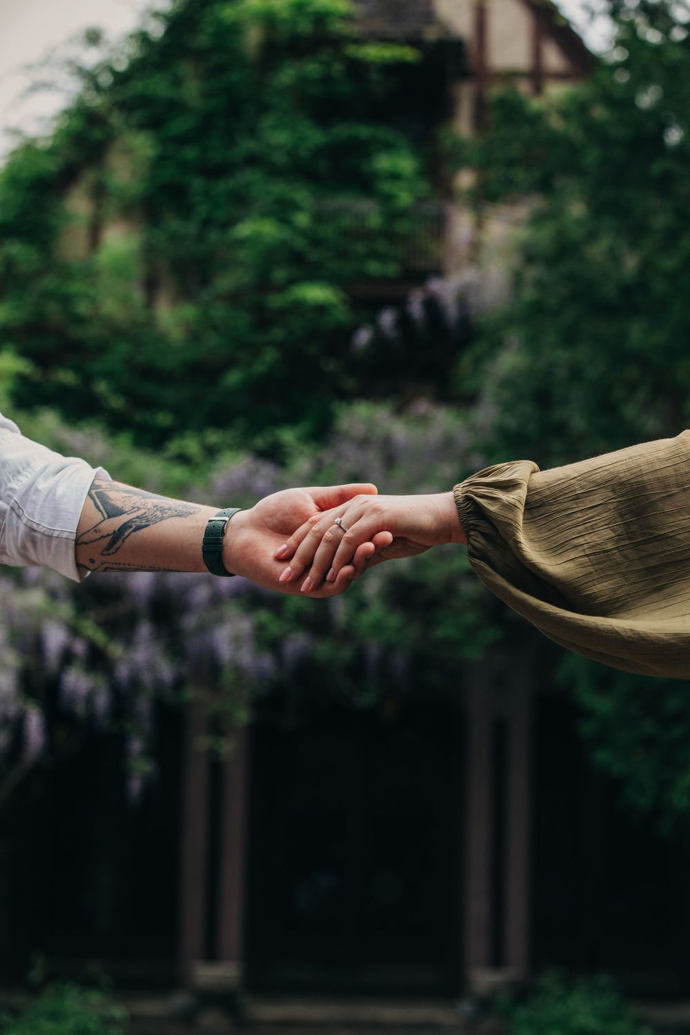 Close-up of hands reaching towards each other against a backdrop of purple wisteria flowers.