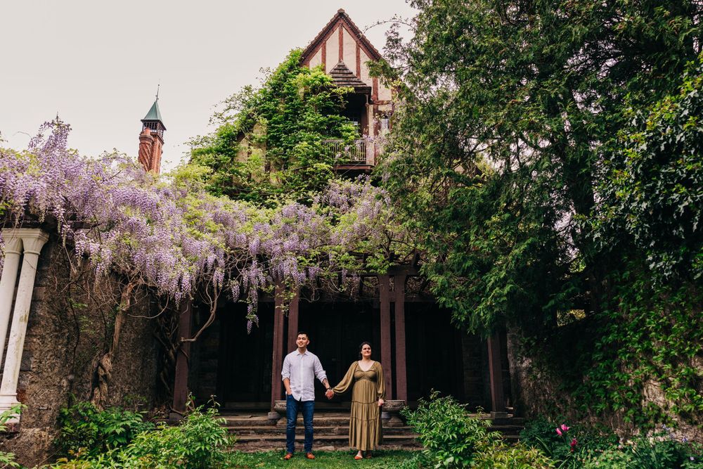 A couple walks through a garden path with blooming wisteria and historic architecture.