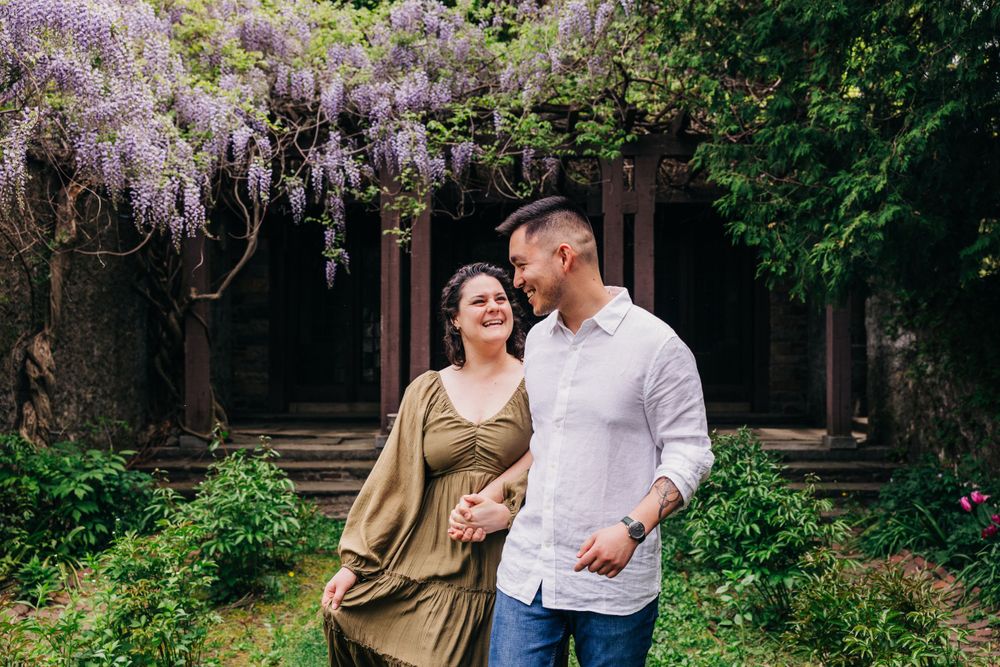 Romantic garden photoshoot among blooming wisteria vines and stone architecture.
