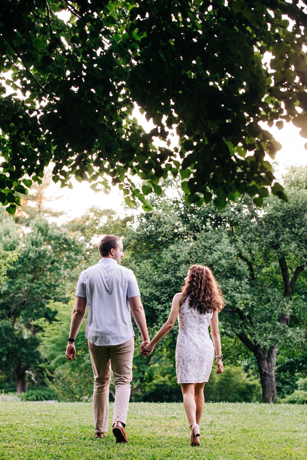 A couple walking hand in hand through a lush green park during golden hour.