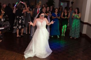 Bride in white dress dancing joyfully at wedding reception with colorful lights.