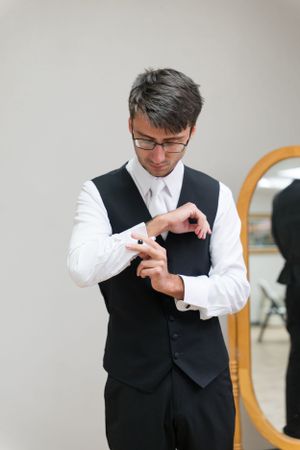 Groom adjusting cufflinks while getting dressed in formal attire.