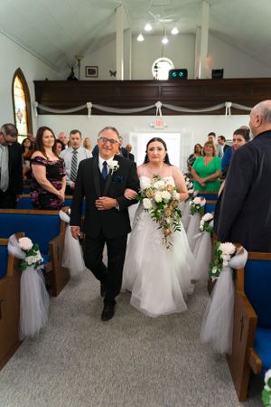 Wedding processional in traditional church with bride in white gown walking down pew-lined aisle.