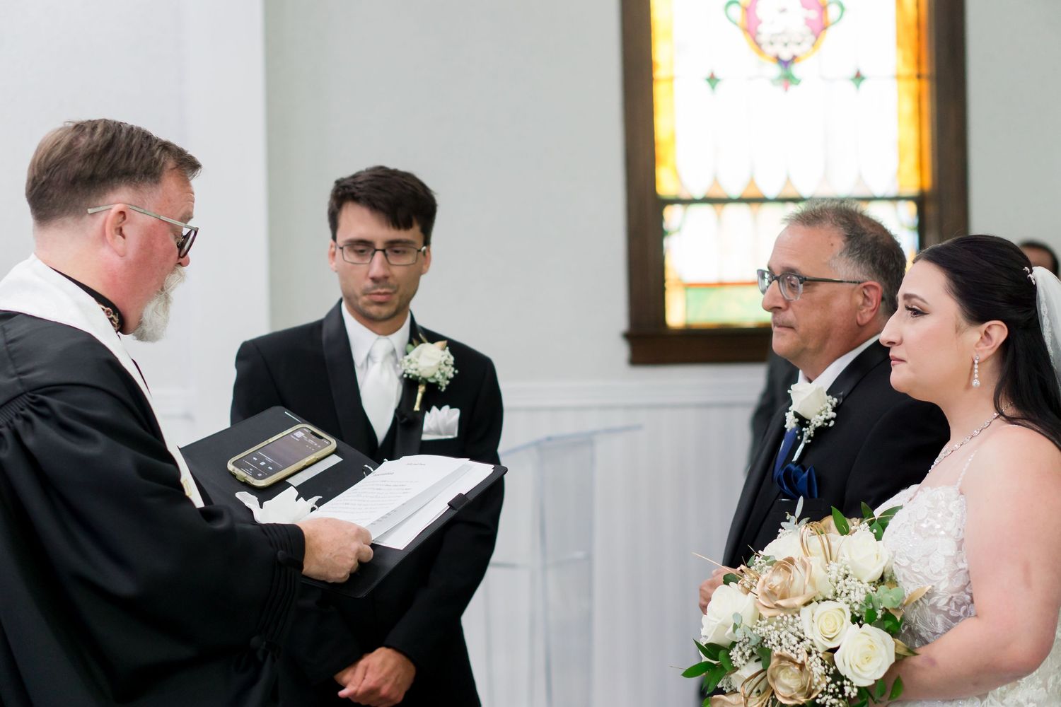 Wedding ceremony in progress inside historic church with stained glass windows.