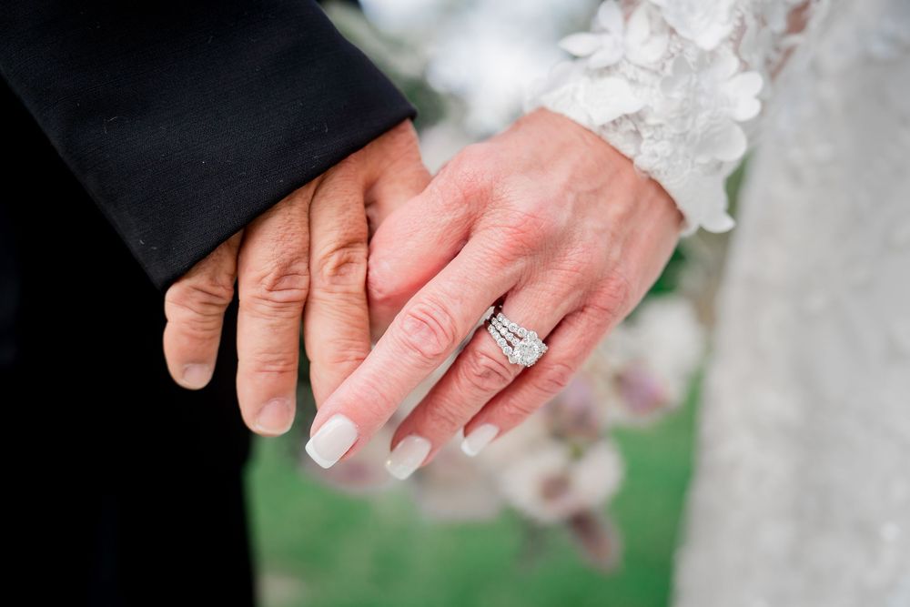 A close-up view of hands displaying a diamond engagement ring against a white lace background.