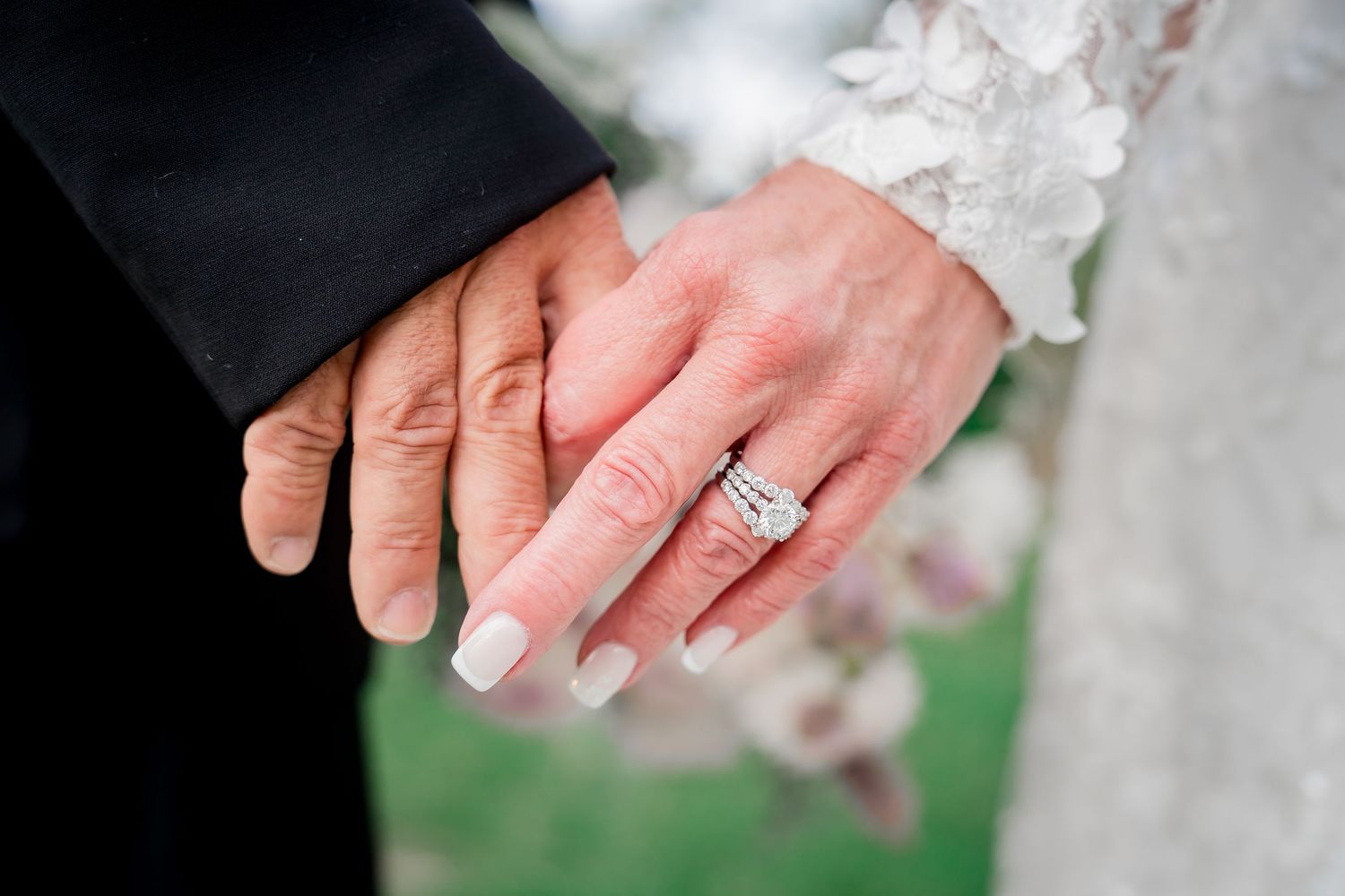 A close-up view of hands displaying a diamond engagement ring against a white lace background.