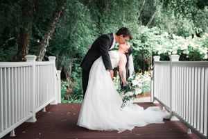 Romantic wedding couple sharing intimate moment on white wooden bridge surrounded by greenery.