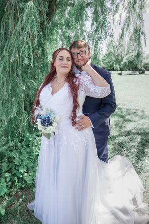 A couple shares romantic moments under weeping willow trees in a garden setting during their wedding celebration.