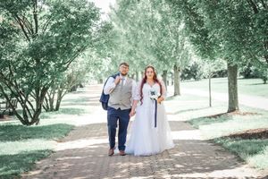 A couple walks hand in hand down a tree-lined path on a sunny summer day.