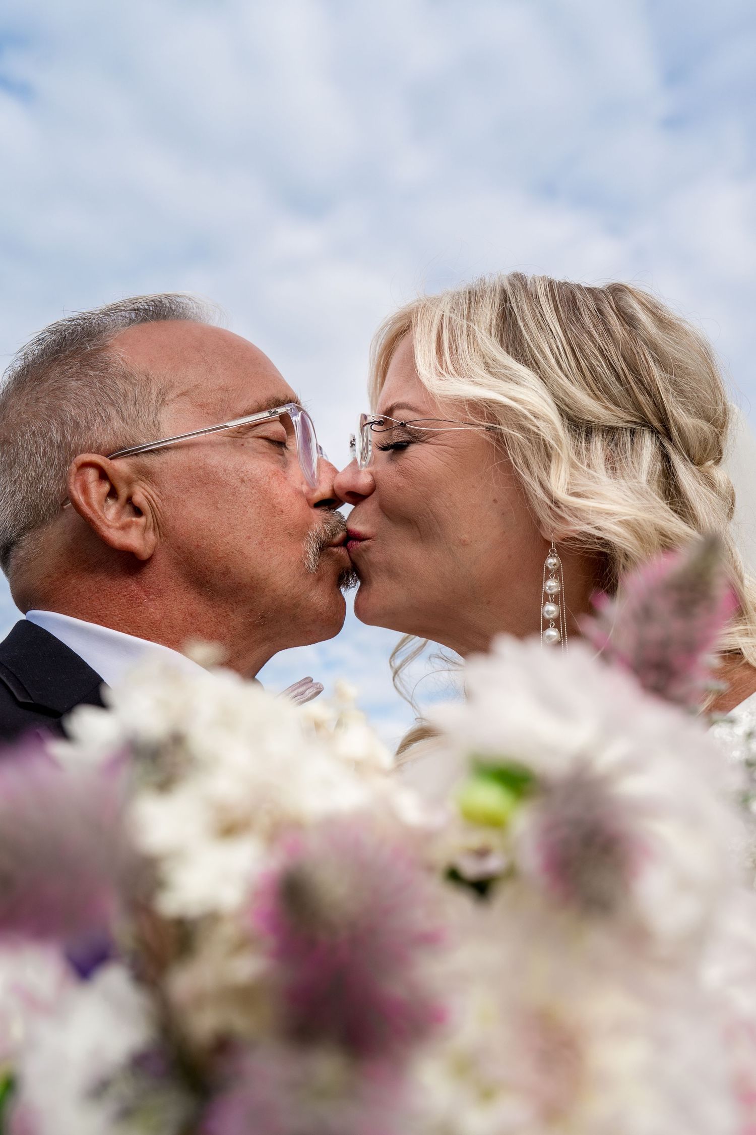 A romantic kiss shared between a couple amidst blooming white and purple flowers on their wedding day.