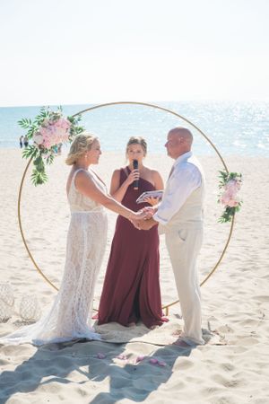 Beach wedding ceremony under circular arch with ocean backdrop and floral decorations.