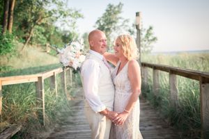 Newlyweds sharing a romantic moment on a wooden boardwalk by the beach at sunset.