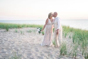 A romantic moment between newlyweds on a sandy beach with dune grass at sunset.