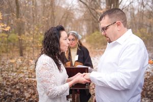 A couple in white attire performs their first dance together in an autumn forest setting.