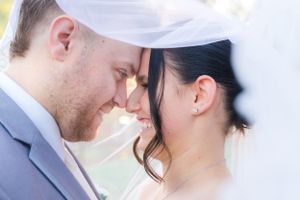 Intimate wedding moment captured under white veil outdoors.