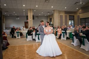 Newlyweds share first dance in elegant reception hall with guests watching.