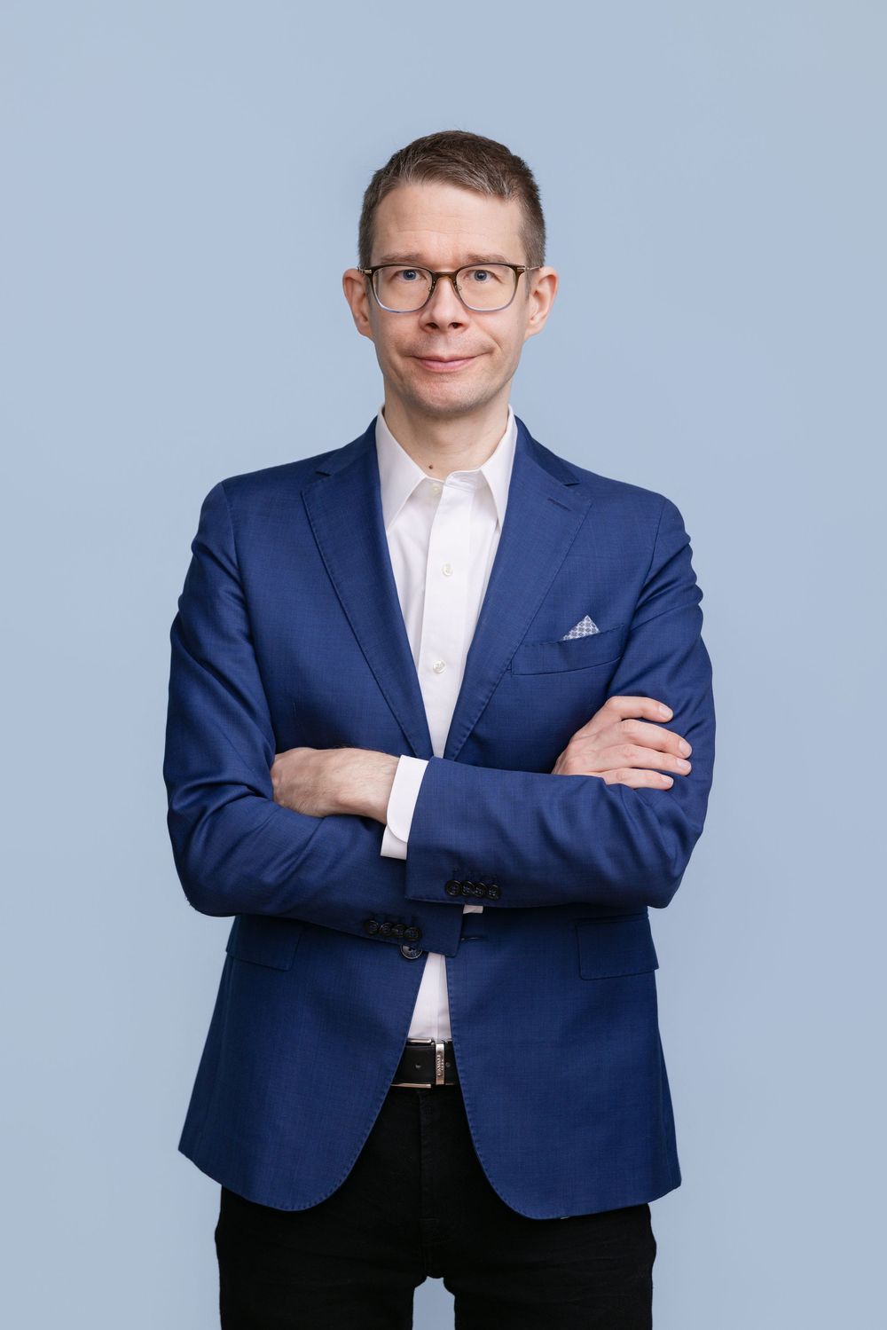 Henkilöstökuva, jossa mies seisoo  sinisessä takissa vaaleansinistä taustaa vasten.