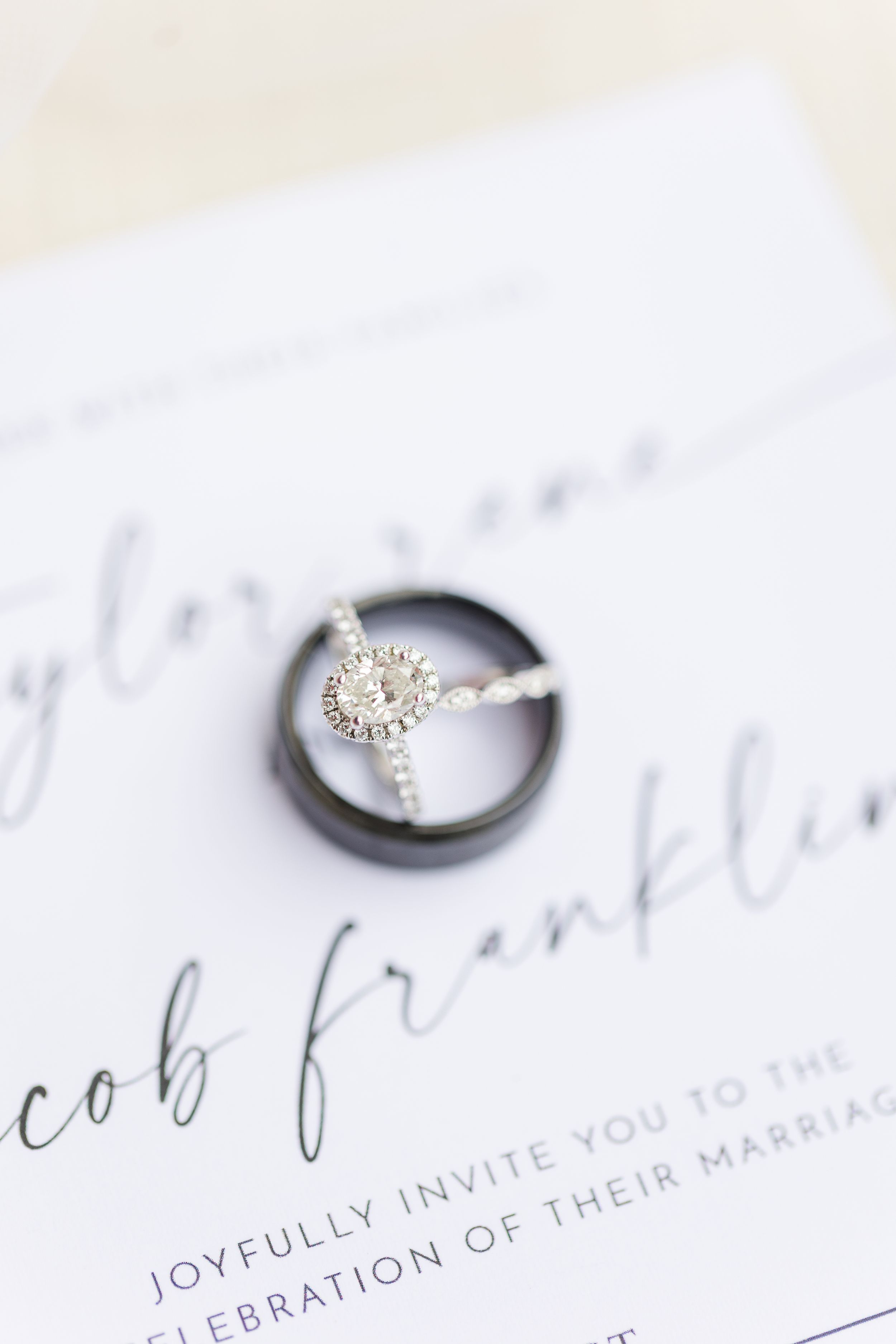 Wedding invitation details with elegant calligraphy and diamond rings on a white surface.
