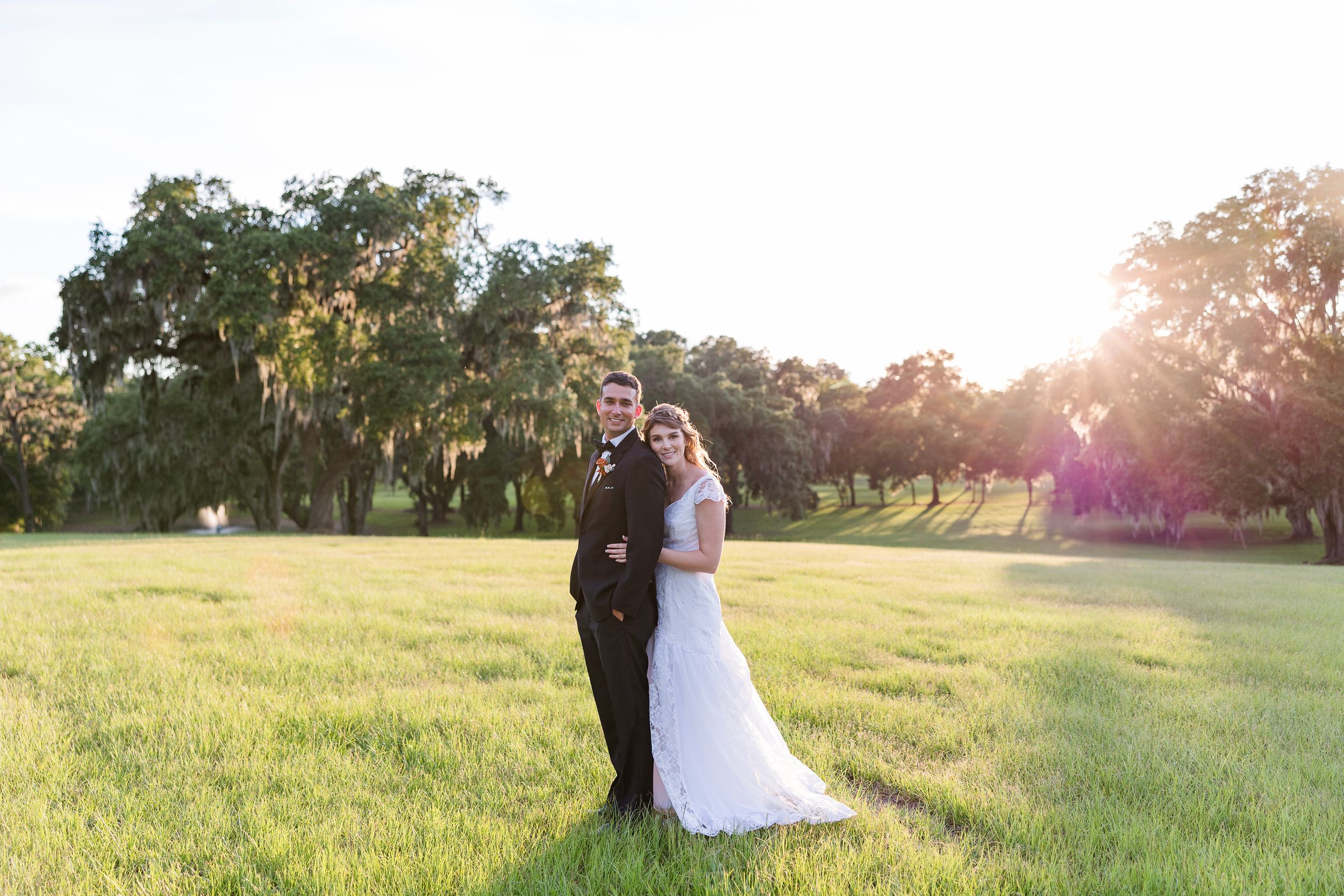 A couple shares a romantic moment in a sunlit field during golden hour at sunset.