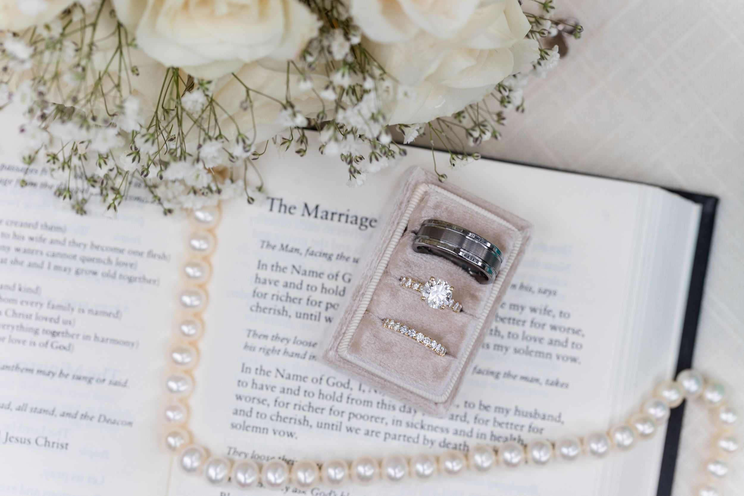 Wedding accessories including pearl necklace and invitation details arranged on white surface.