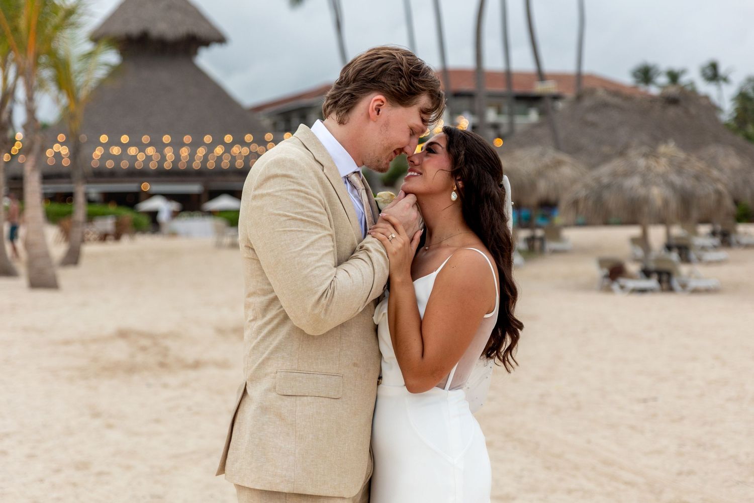 Bride and groom in elegant wedding attire sharing a romantic moment on a tropical beach resort.