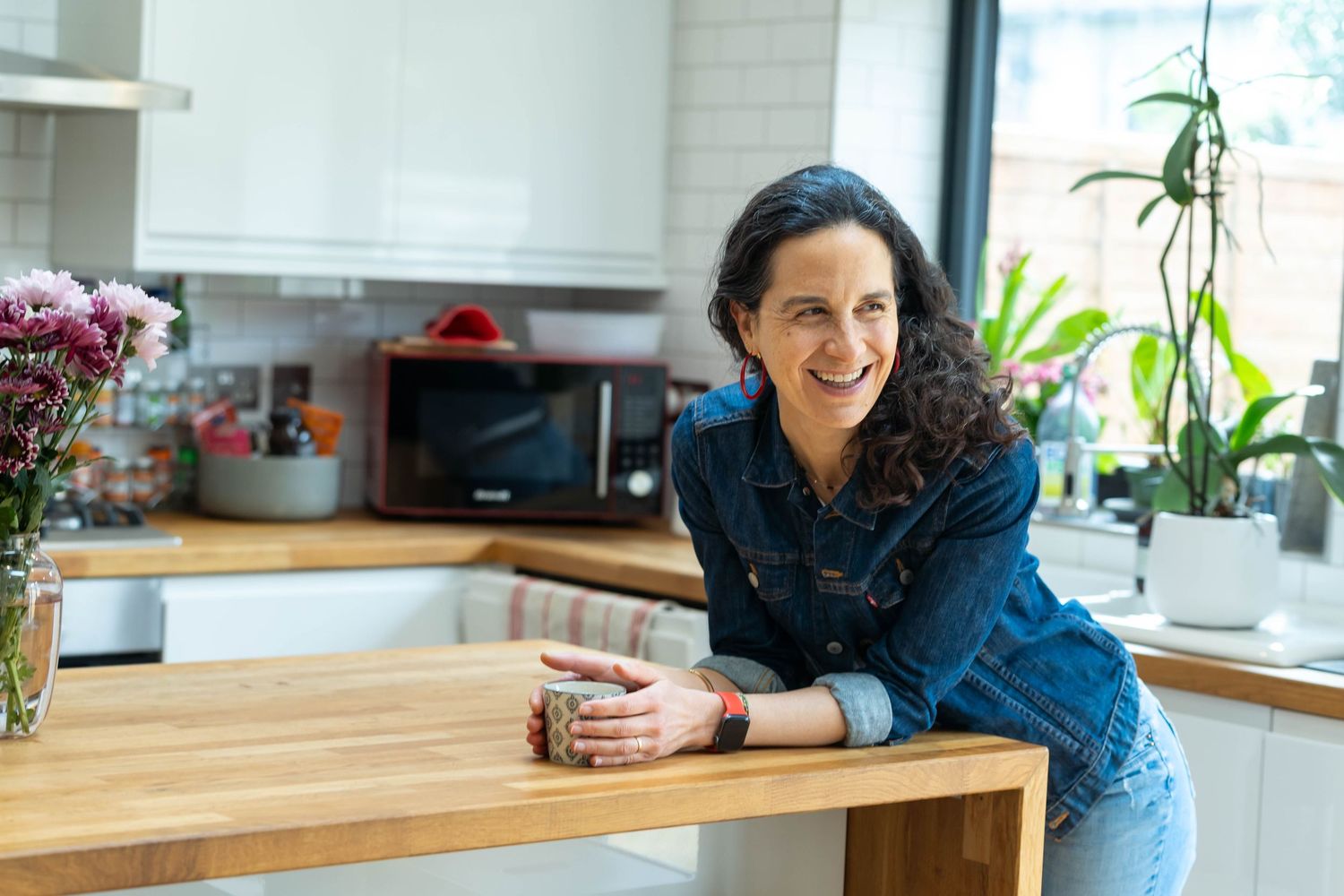 Personal branding shoot brighton a woman stands in her kitchen in a denim jacket holding a cup of tea