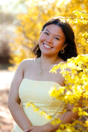 Smiling young woman in yellow strapless dress poses outdoors among bright autumn yellow foliage.