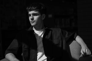 A group of youths stand in a lineup against a black wall, wearing casual attire with dark shadows cast on them.