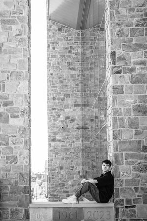 A person sits alone on a stone ledge between two massive stone walls of an ancient building or castle.