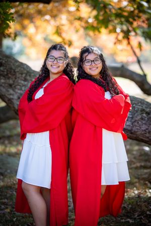 Two people wearing matching red and white outfits pose under autumn trees with golden sunlight filtering through the leaves.