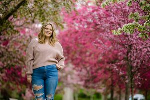 Beautiful spring cherry blossoms create pink canopy over scenic garden path with person in casual attire.