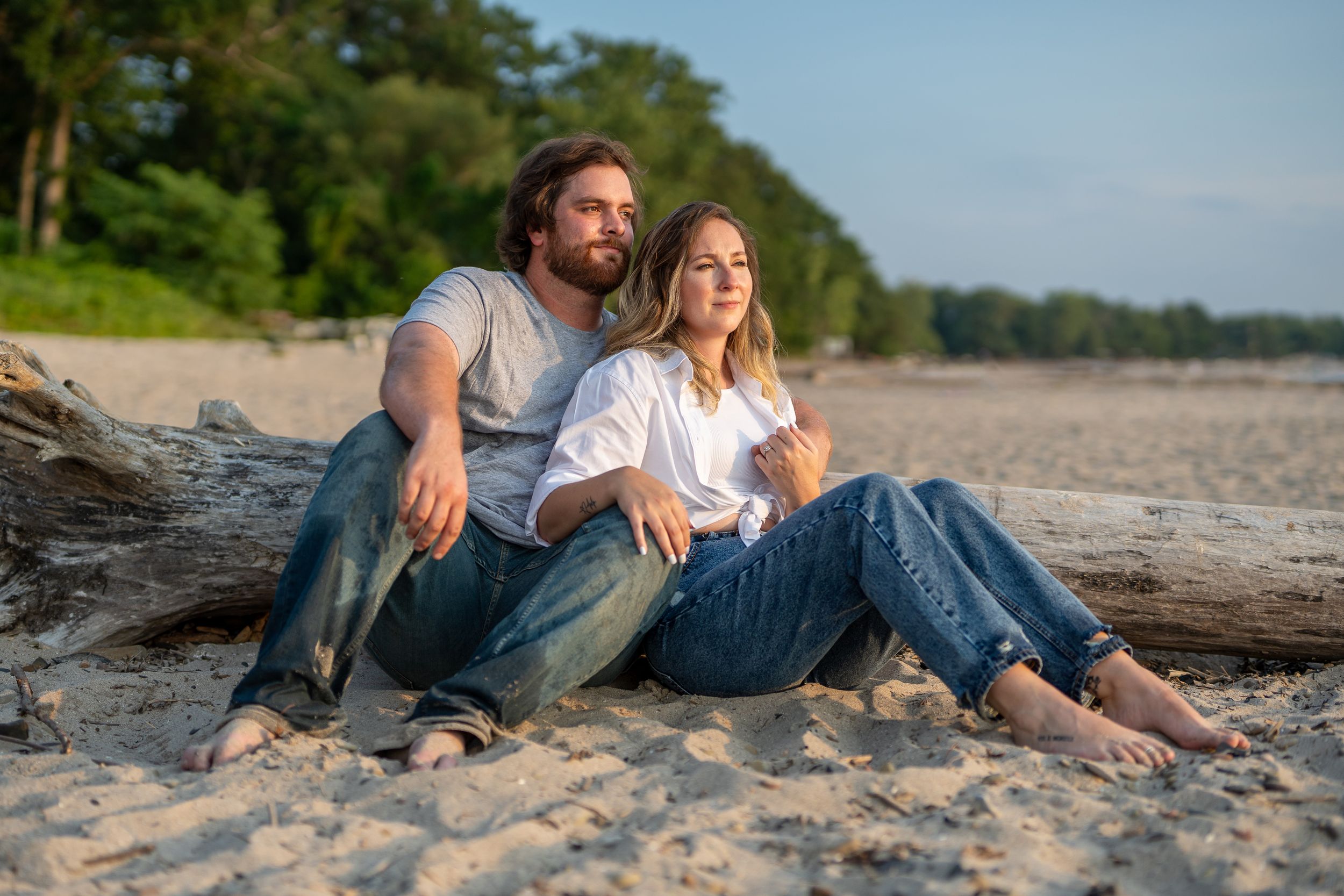 Couple relaxing together on driftwood at sandy beach during sunset.