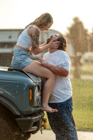 A couple shares a playful moment together while sitting on a vintage truck in golden hour sunlight.