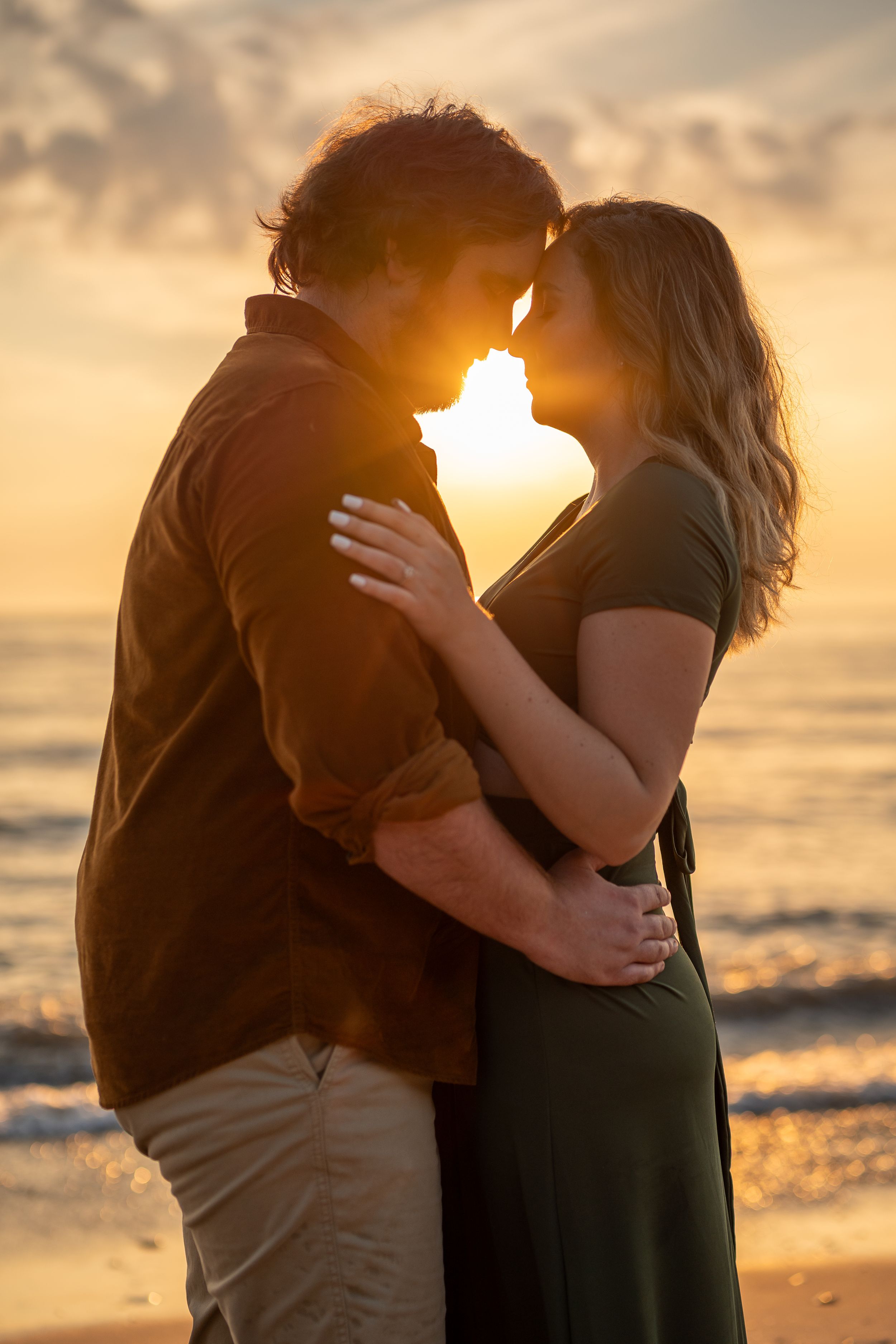 Intimate sunset beach portrait with warm golden light and ocean backdrop.