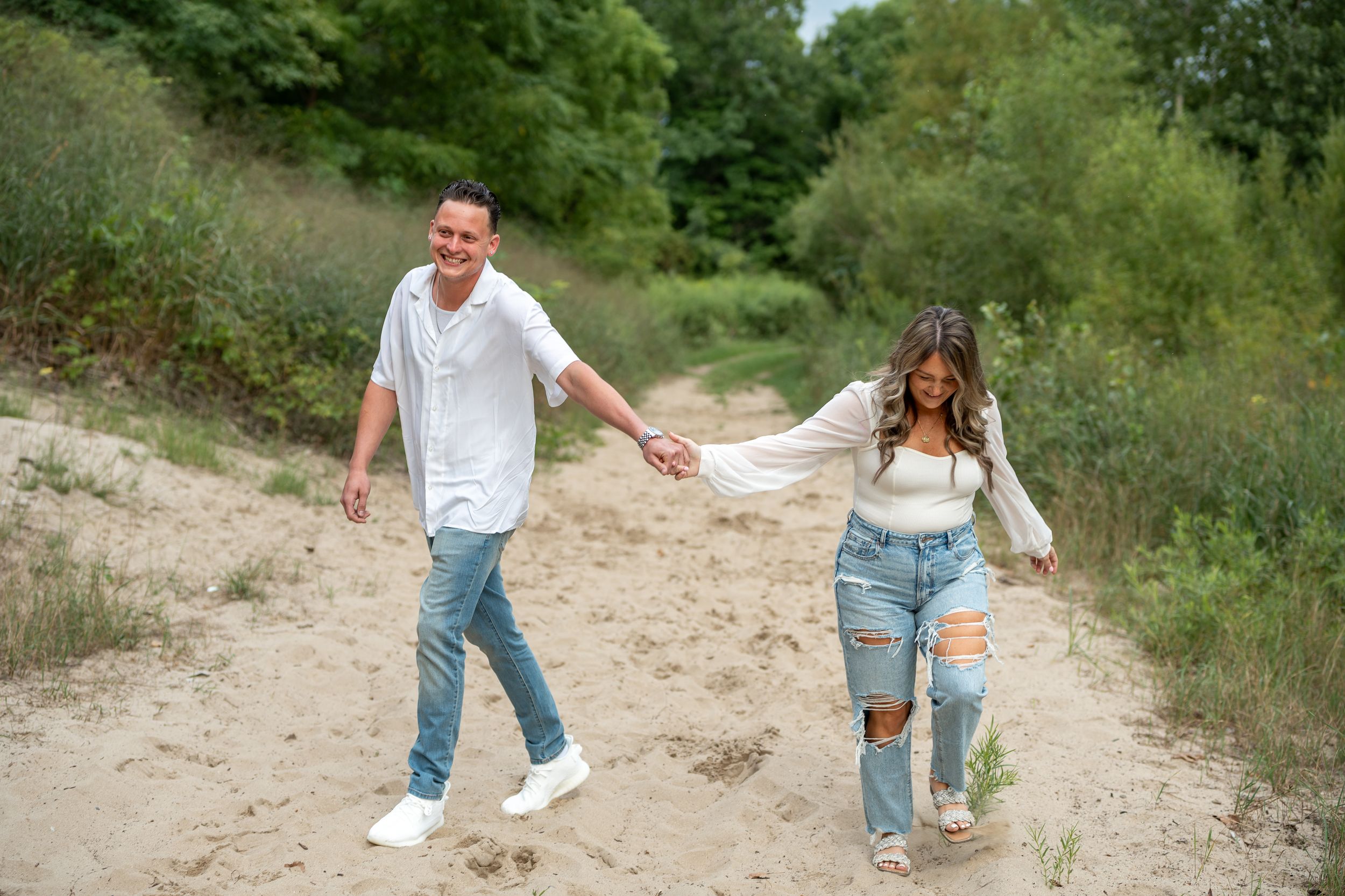 Couple holding hands while walking along scenic dirt path surrounded by greenery.