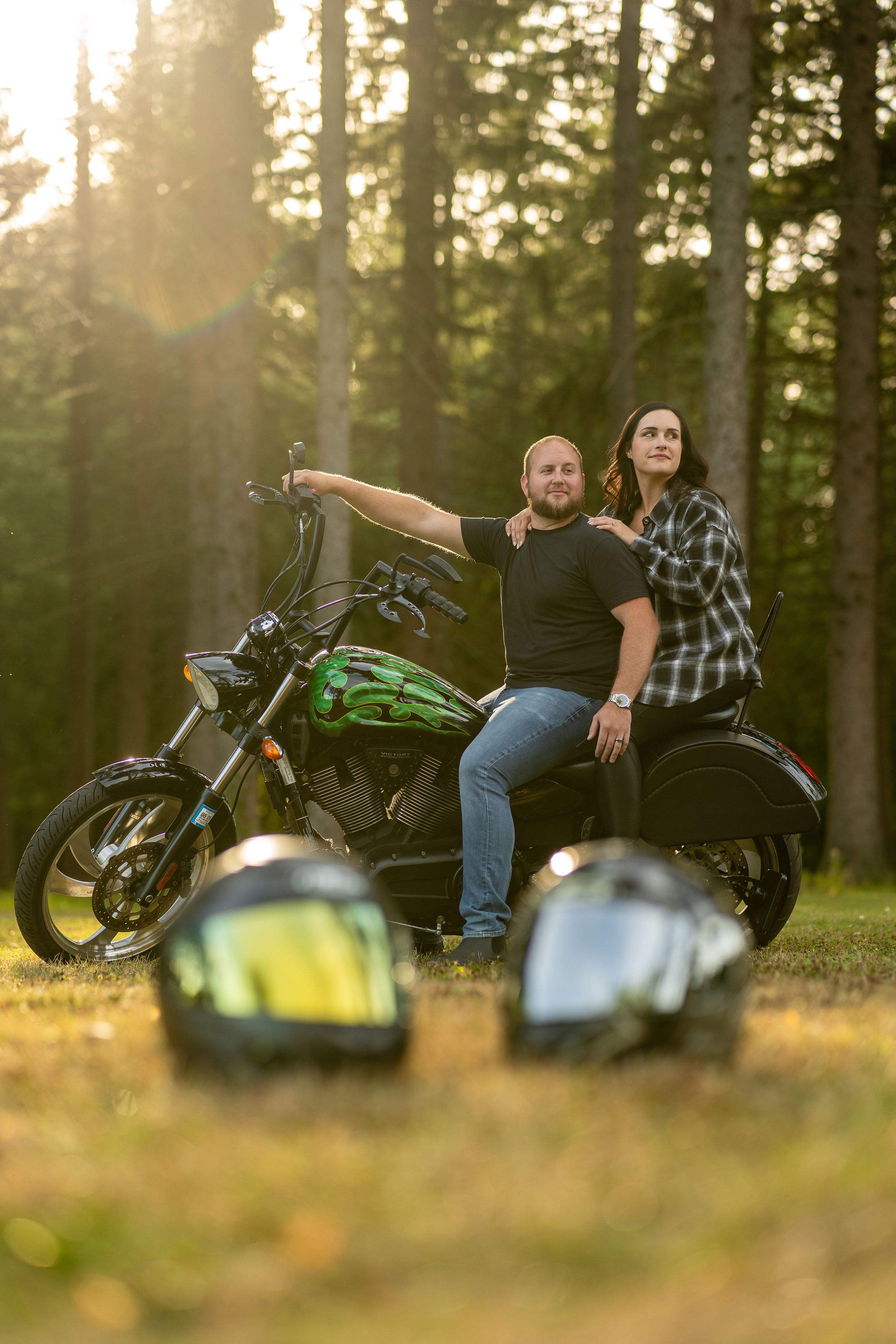 Two motorcycles parked in a forest clearing during golden hour sunset with riders relaxing in background.