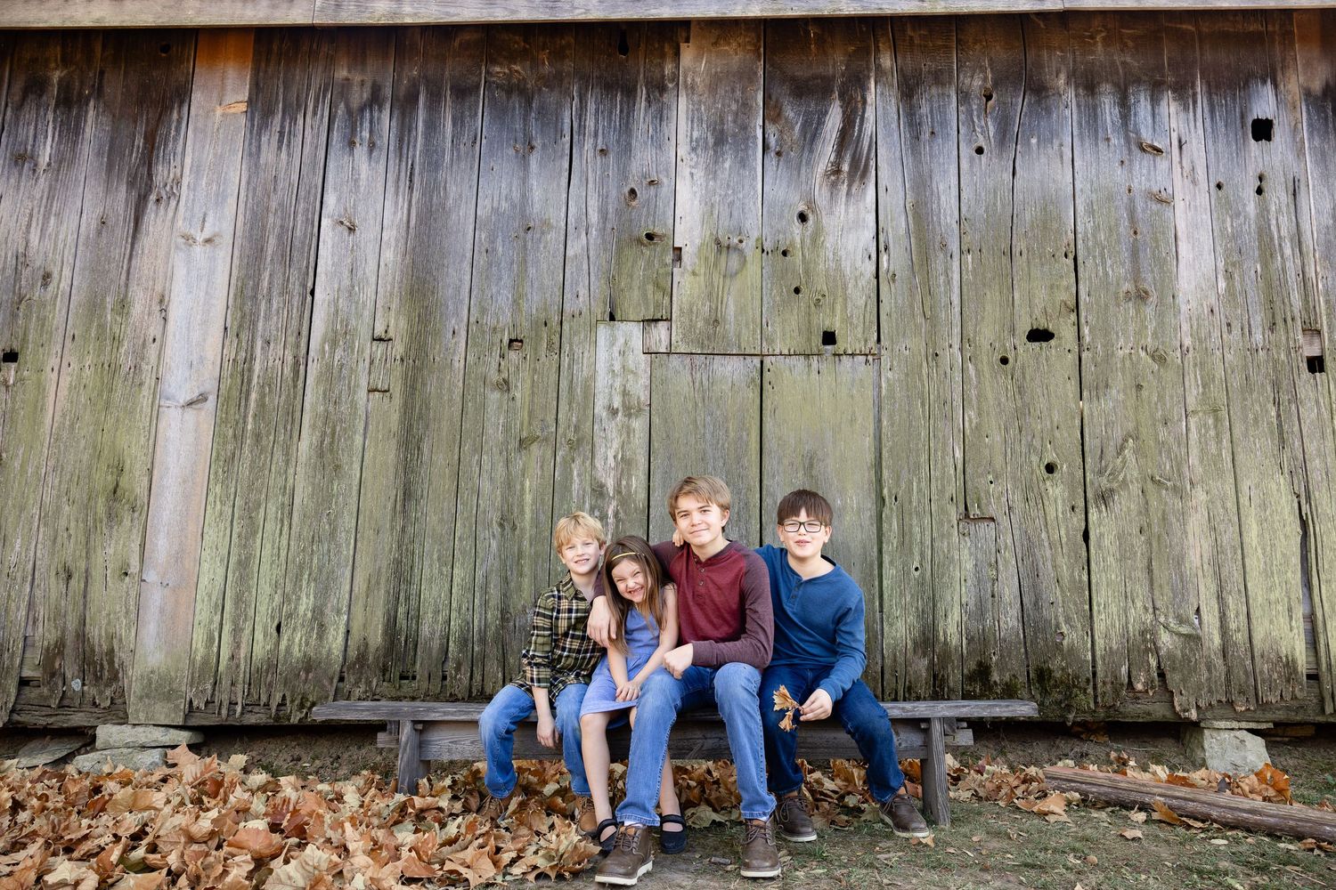 A family of five, including parents and three children, sitting together on a wooden structure in a rural outdoor setting.